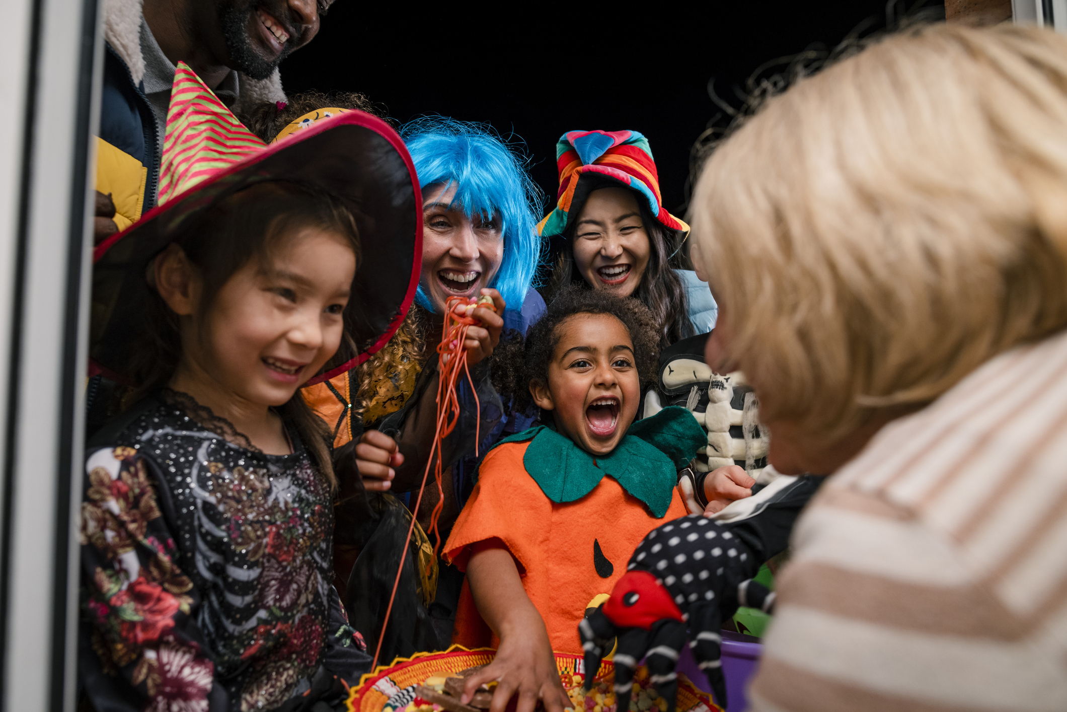 Taken from inside a residential house, two families wearing fancy dress, out trick or treating in North East England during halloween. They are taking sweets off a plate that an unrecognisable woman is holding.